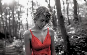 black and white photo of a sad woman standing in a forest wearing a red dress
