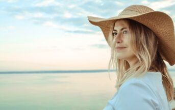 30-year-old woman wearing a large beach hat looking out over the ocean