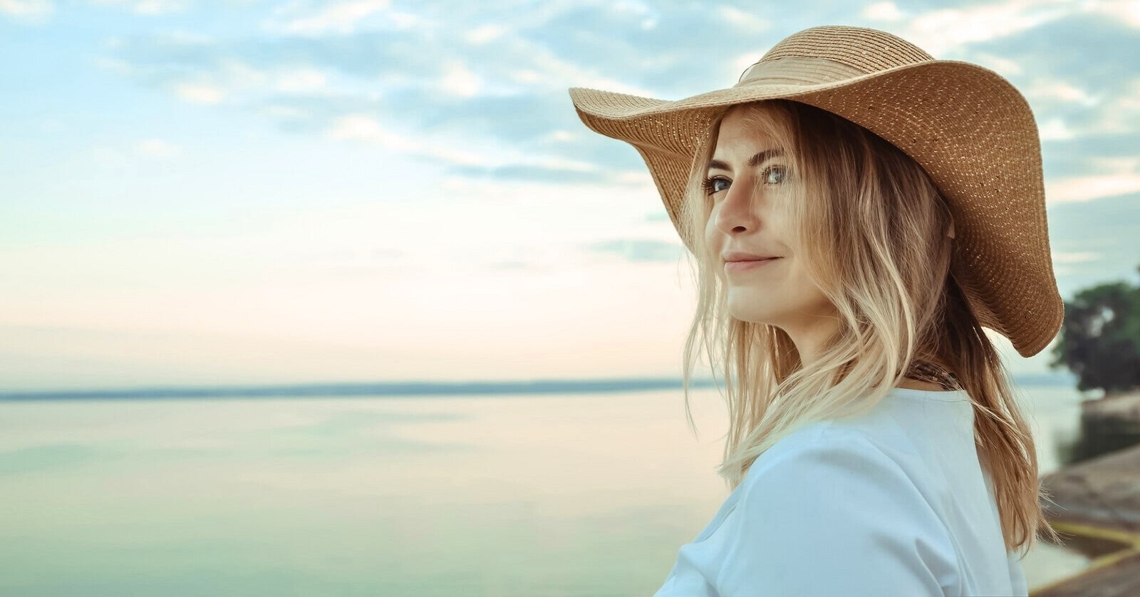 30-year-old woman wearing a large beach hat looking out over the ocean