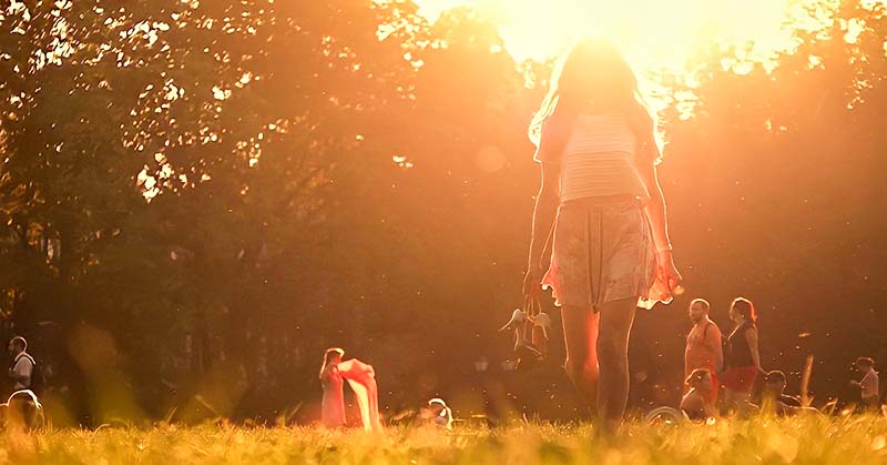 woman walking barefoot with sun in background - concept of free spirit