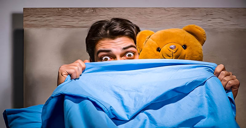 man with teddy bear hiding behind duvet - demonstrating immaturity