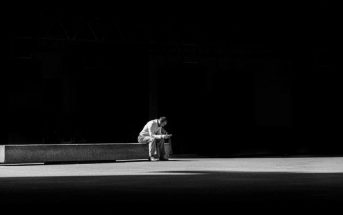 man sitting on concrete bench against black background indicating a simplification of his life