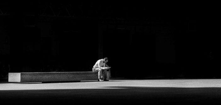 man sitting on concrete bench against black background indicating a simplification of his life