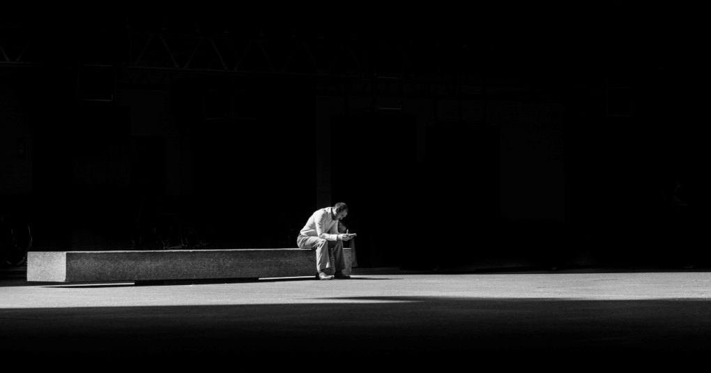 man sitting on concrete bench against black background indicating a simplification of his life