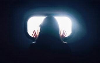 woman in darkness looking out of window - signifying loneliness