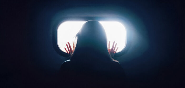 woman in darkness looking out of window - signifying loneliness