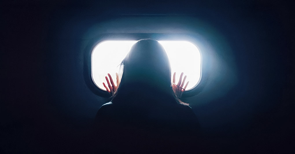 woman in darkness looking out of window - signifying loneliness