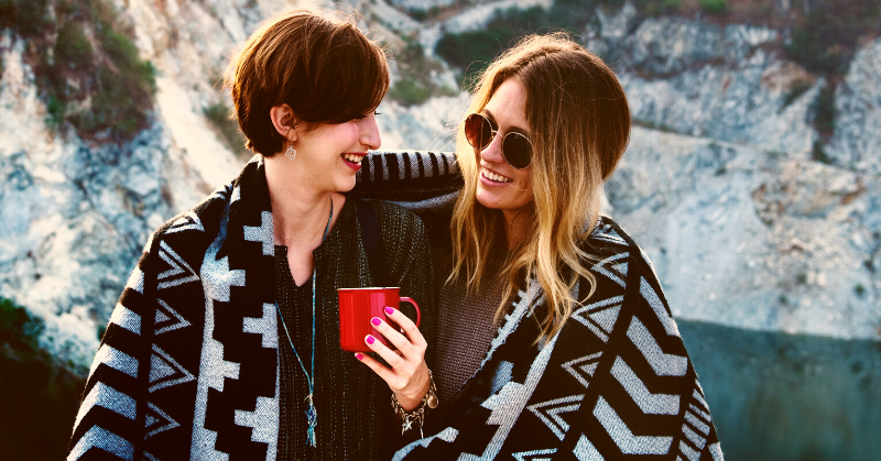 good friends sharing blanket and hot drink