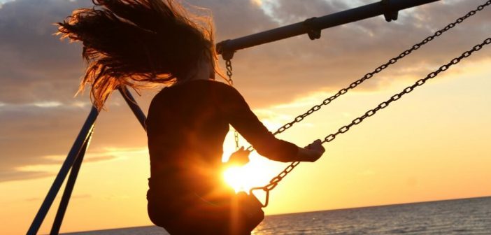 silhouette of woman on swing with sunset in background