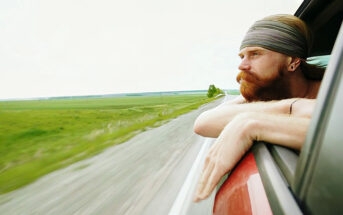 young man with beard looking out car window