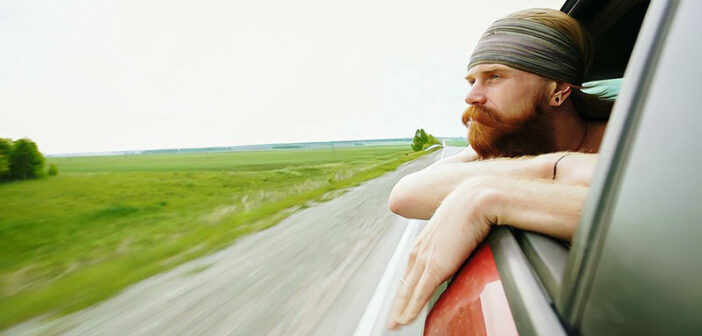 young man with beard looking out car window