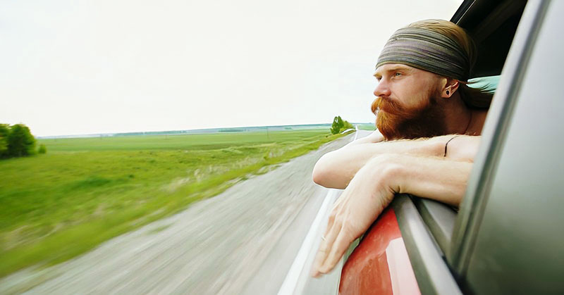 young man with beard looking out car window
