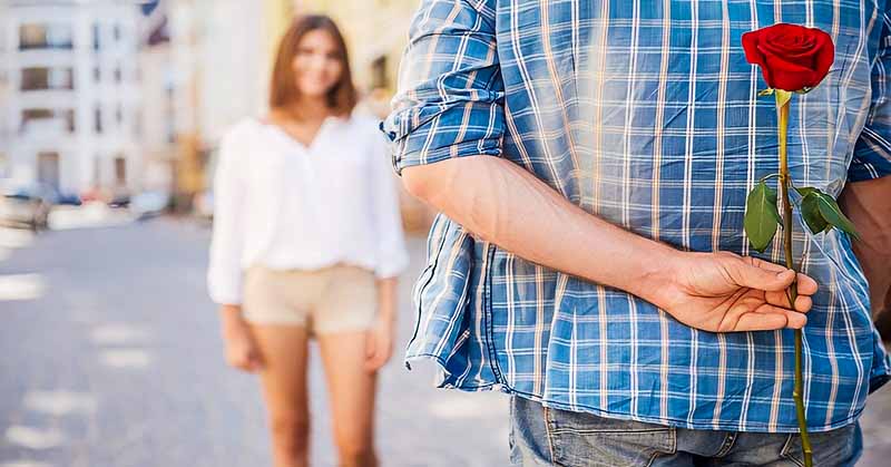 man holding rose behind back for woman to signify unrequited love