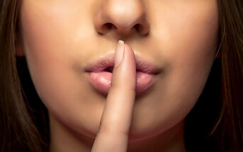 woman with finger pushed against lip in shhh motion - concept of white lies