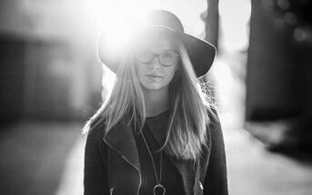 black and white photo of woman in hat on sunny street