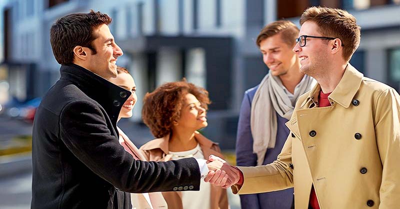 two men sharing a handshake with friends in the background