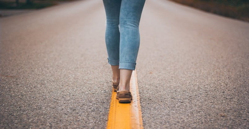 legs and feet of woman walking down middle of road