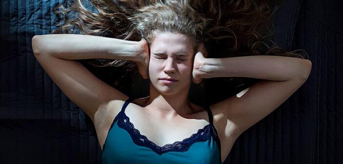 young woman lying down with hands over ears trying to stop her negative thoughts