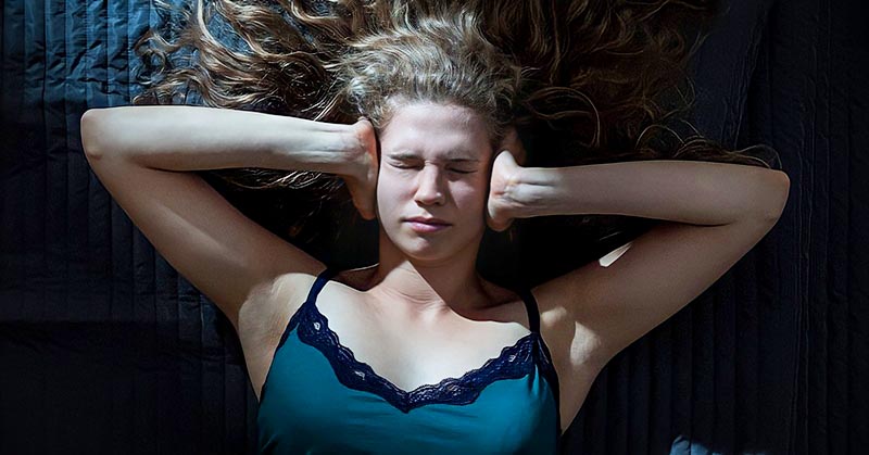 young woman lying down with hands over ears trying to stop her negative thoughts
