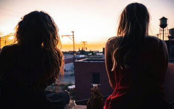 two friends talking while watching a sunset over a town