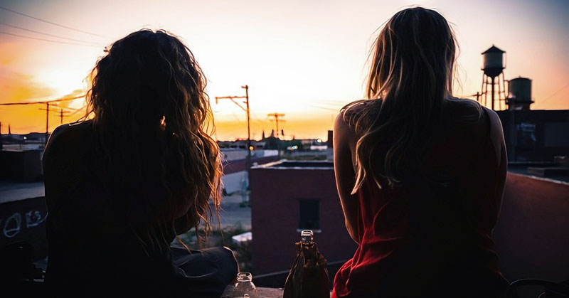 two friends talking while watching a sunset over a town