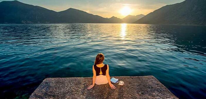 woman sitting on pier overlooking sunrise - concept of being patient