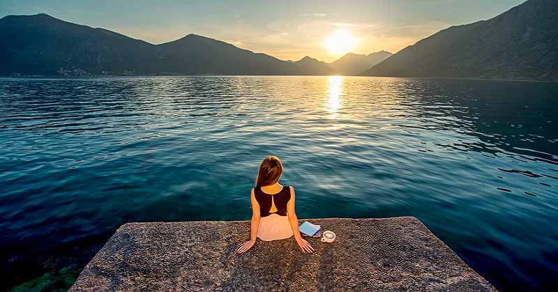 woman sitting on pier overlooking sunrise - concept of being patient