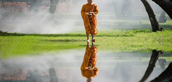 A Buddhist monk walking with reflection in water - concept of Nirvana