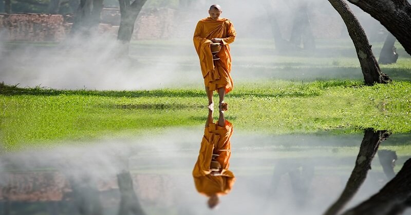 A Buddhist monk walking with reflection in water - concept of Nirvana