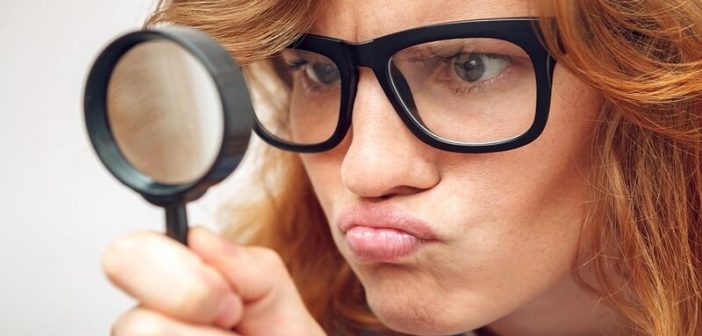 young woman looking through magnifying glass - illustrating being detail oriented