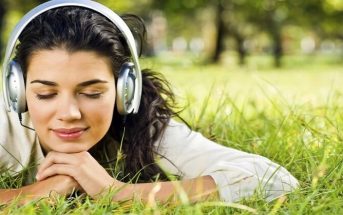 young woman lying on grass with headphones on illustrating music therapy
