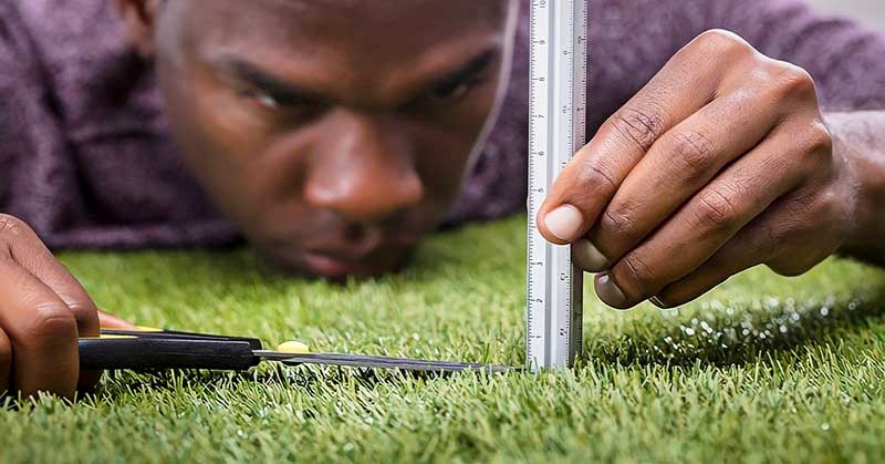 perfectionist man cutting grass with scissors and ruler