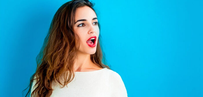 young woman with open mouth as if about to speak, isolated against blue background