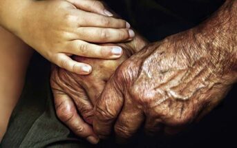 closeup of child holding elderly person's hands and showing them compassion