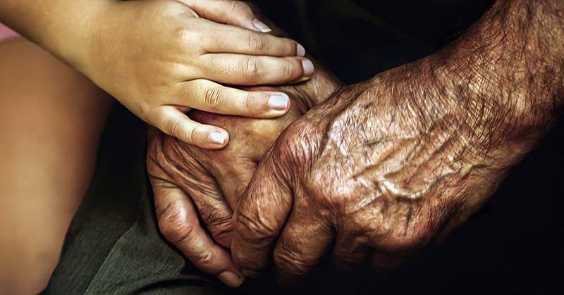 closeup of child holding elderly person's hands and showing them compassion