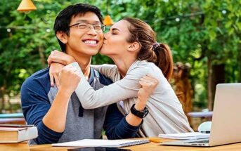 young Asian man being kissed on cheek by attractive young woman - illustrating getting out of the friend zone