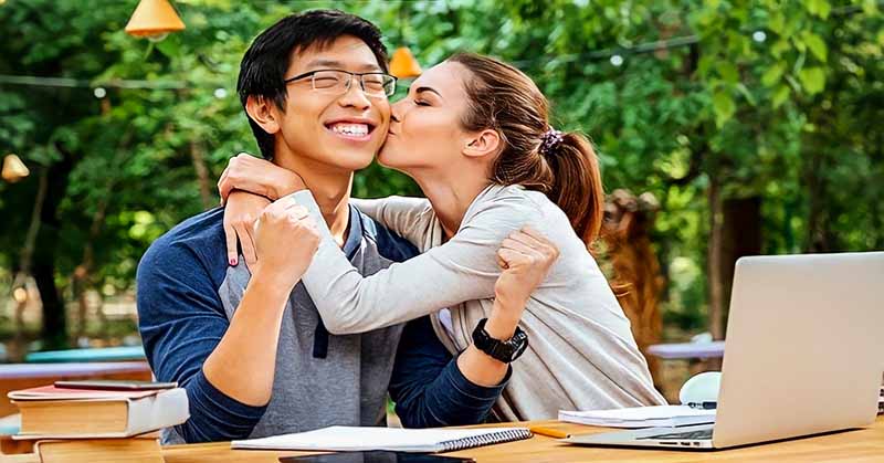 young Asian man being kissed on cheek by attractive young woman - illustrating getting out of the friend zone