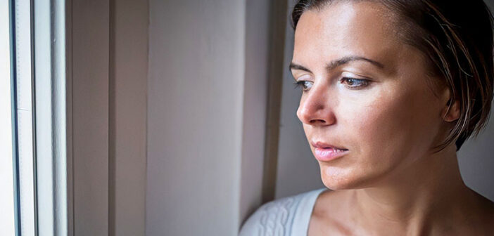 sad pensive woman looking out of window illustrating self-denial