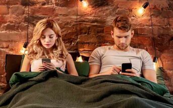 couple sitting in bed staring at their phone illustrating effects of social media on relationships