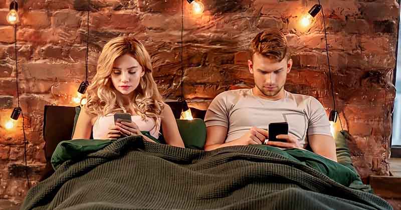 couple sitting in bed staring at their phone illustrating effects of social media on relationships