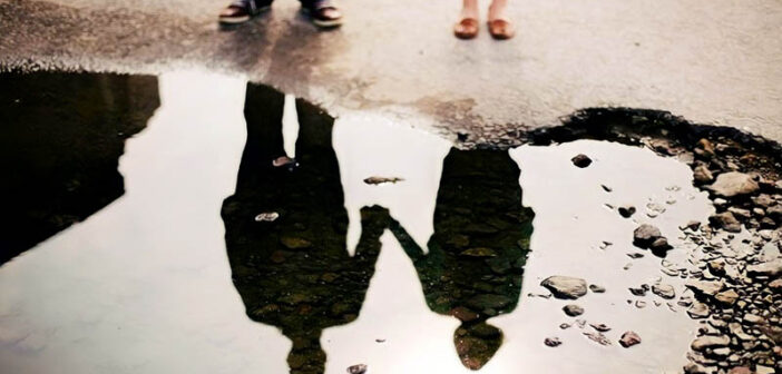 reflection in a puddle of couple holding hands illustrating a situationship