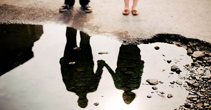 reflection in a puddle of couple holding hands illustrating a situationship