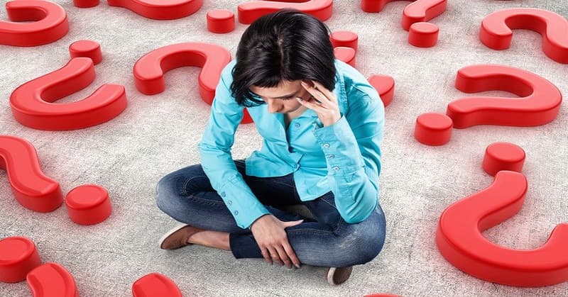 young anxious girl sitting on floor surrounded by question marks illustrating decision anxiety