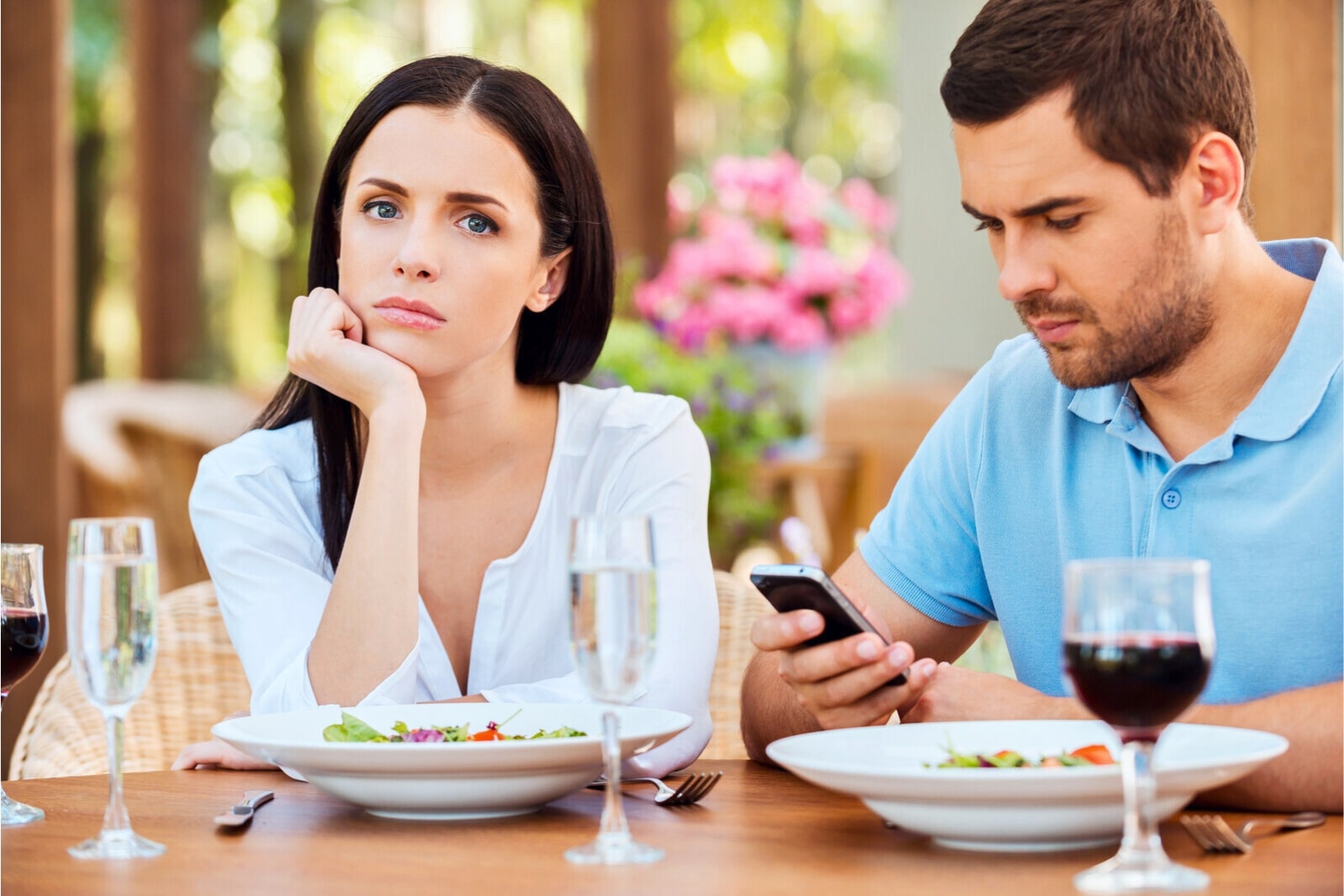 man distracted by his phone while his date looks on unimpressed