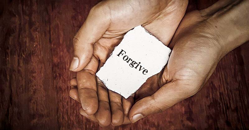 hands held together holding piece of paper with forgive written on it