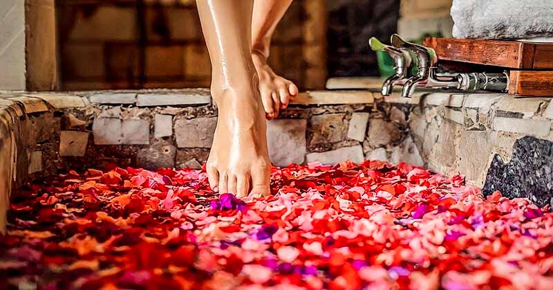 woman stepping into bath with rose petals - example of how being selfish is good