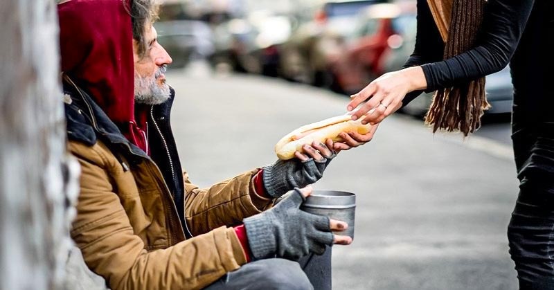 woman handing food to homeless person - illustrating being generous