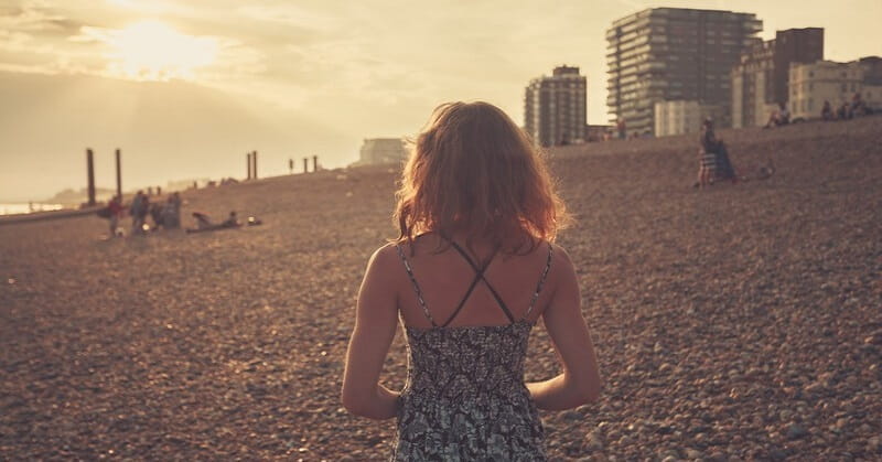 woman walking alone on beach at sunset