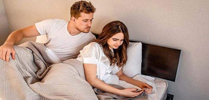 boyfriend looking over girlfriend's shoulder at her text messages - illustrating a partner with trust issues