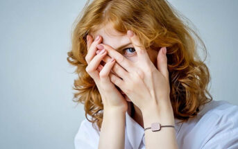 red-haired woman with eyes peeping through fingers illustrating a fear of being judged